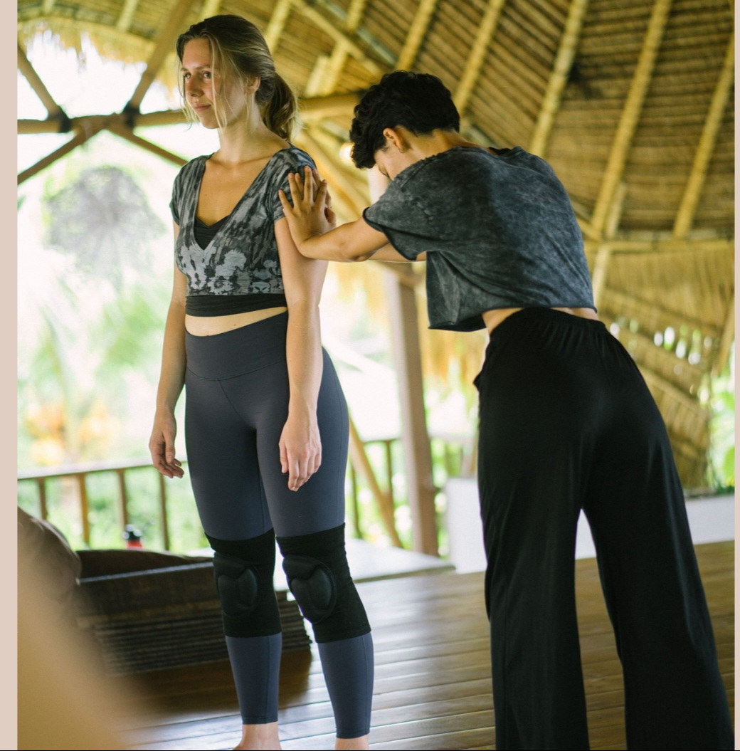 Aalia adjusting a student's shoulders in a bamboo studio
