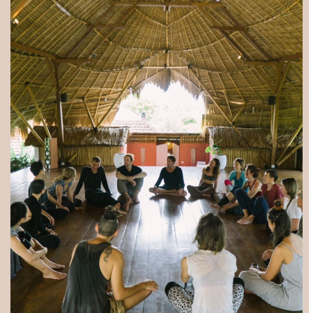 A large circle of dancers sitting under a thatched roof