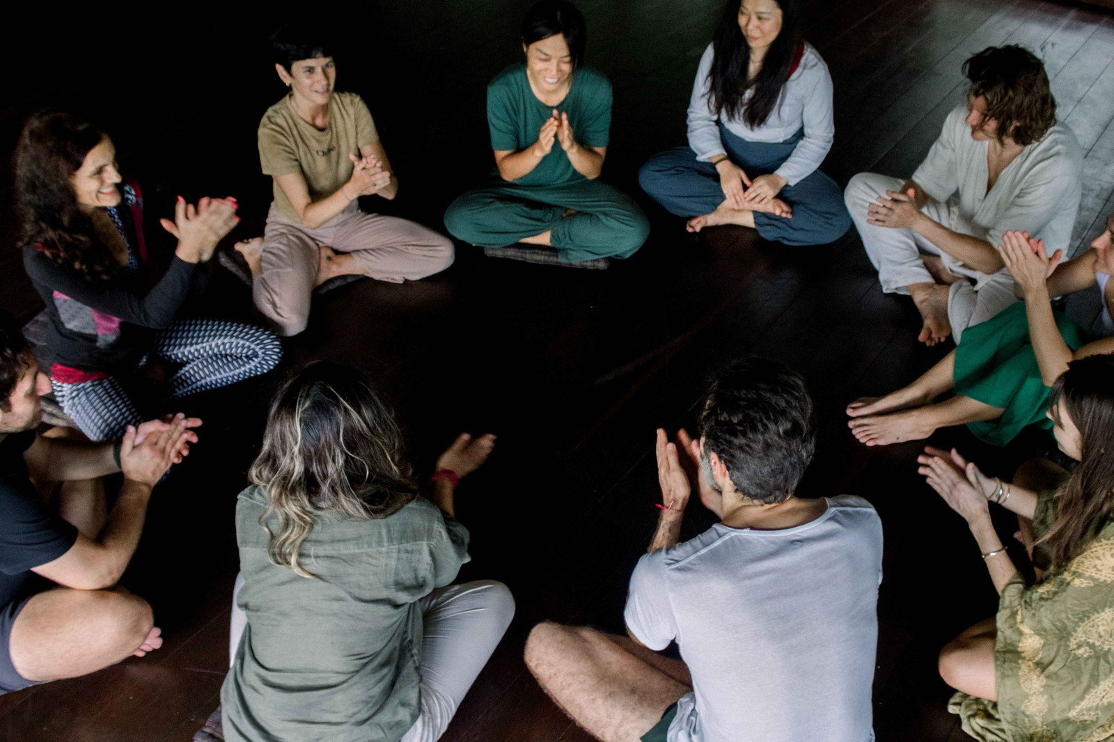 Dancers sitting in a circle on a dark wooden floor, clapping together