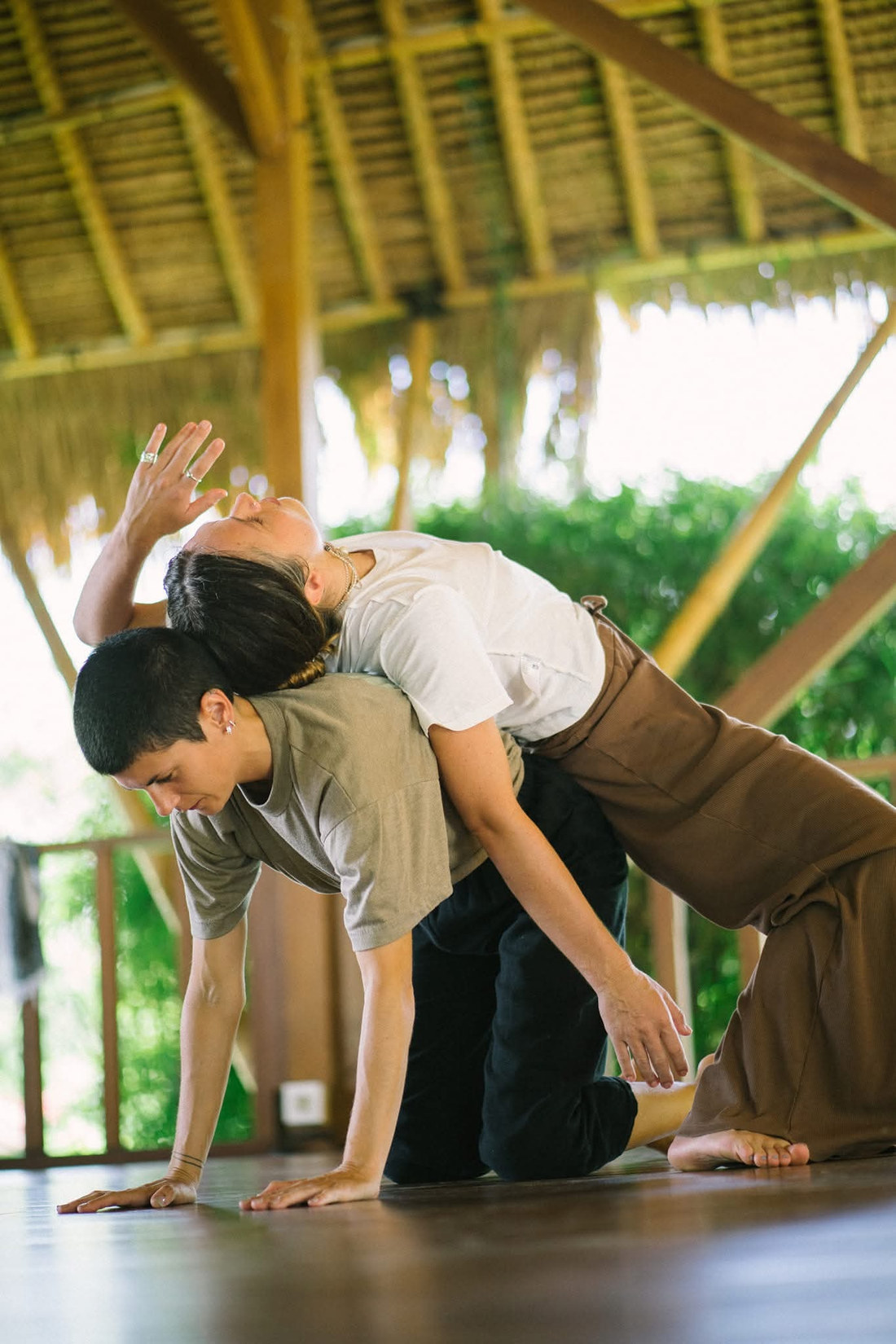 Two dancers in a supported lean under a thatched roof