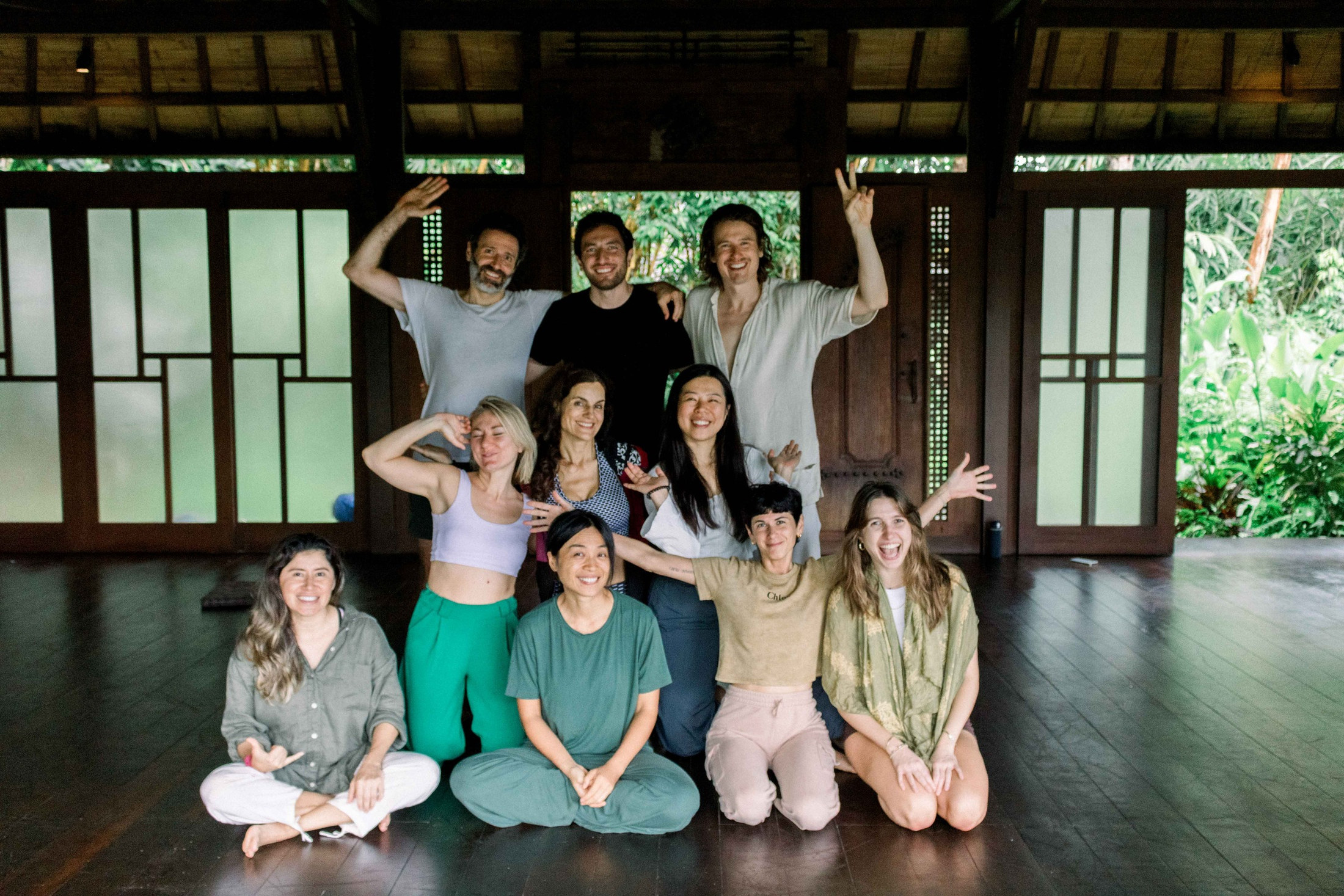 A joyful group of Momentum dancers in a dark wooden studio in Bali, arms raised