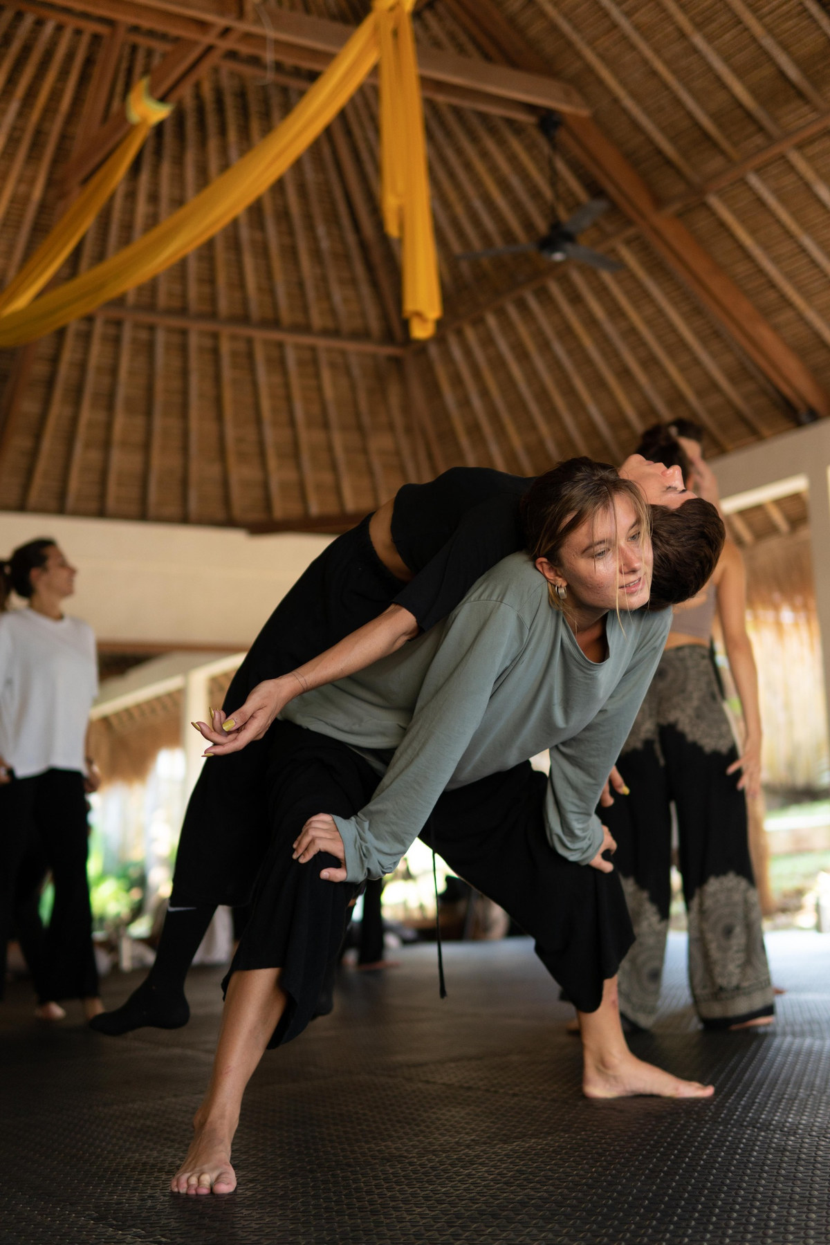 Two dancers in a counterbalance lift under a bamboo roof
